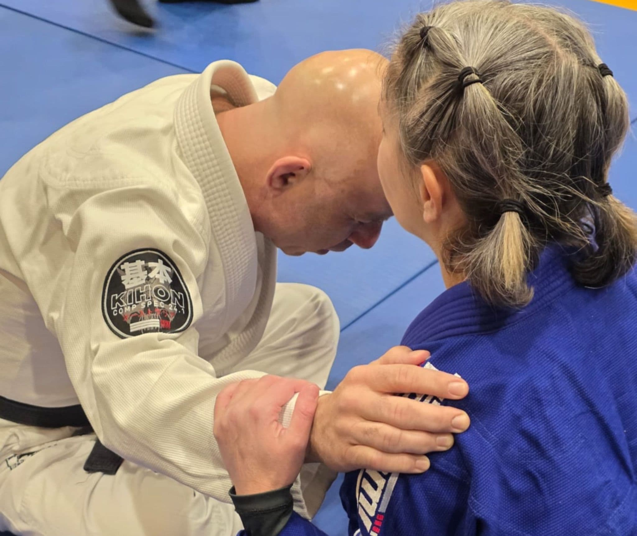 Two Brazilian Jiu-Jitsu competitors kneeling together on the mats with heads bowed before competition.